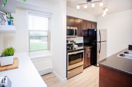 Kitchen featuring stainless steel appliances, dark wood-finish cabinetry, track lighting, and a dual basin sink - #201 1070 Mcconachie Bv Nw, Edmonton, AB 