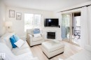 Bright living area featuring wood-finish flooring, a white mantel with a faux fireplace insert, and a sliding glass door opening to an outdoor balcony - #201 1070 Mcconachie Bv Nw, Edmonton, AB 