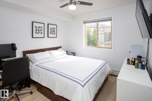 Ceiling fan with integrated lighting, window with light-colored framing, wood-finish flooring, white walls, and a wall-mounted radiator - #201 1070 Mcconachie Bv Nw, Edmonton, AB 