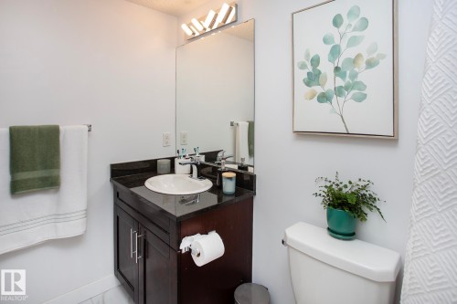 Vanity with a dark countertop and undermount sink, large wall-mounted mirror, and contemporary light fixture - #201 1070 Mcconachie Bv Nw, Edmonton, AB 