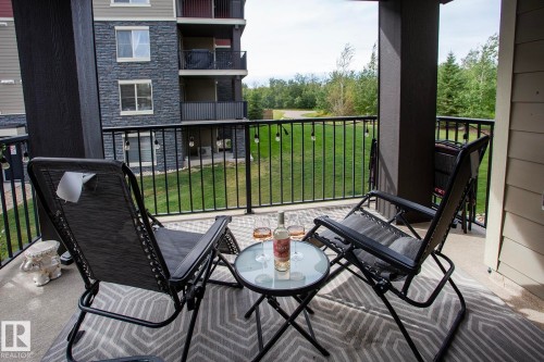Covered outdoor patio with a concrete surface, black metal railings, and a green landscape beyond - #201 1070 Mcconachie Bv Nw, Edmonton, AB 