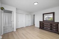 Bright room featuring light wood-finish flooring, multiple white bi-fold closet doors, a ceiling-mounted light fixture, and a partial bathroom with tiled flooring - 