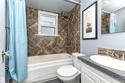 Bathroom featuring a white bathtub, tiled shower surround, window with frosted glass, and a vanity with an integrated sink - 10930 80 Avenue Nw, Edmonton, AB 