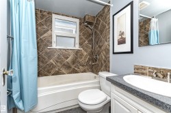 Bathroom featuring a white bathtub, tiled shower surround, window with frosted glass, and a vanity with an integrated sink - 
