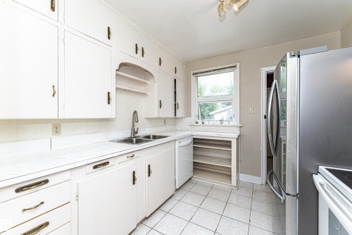 White cabinetry, white countertops, dual basin stainless steel sink, built-in shelving, and tile flooring - 10930 80 Avenue Nw, Edmonton, AB 
