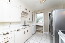 White cabinetry, white countertops, dual basin stainless steel sink, built-in shelving, and tile flooring - 