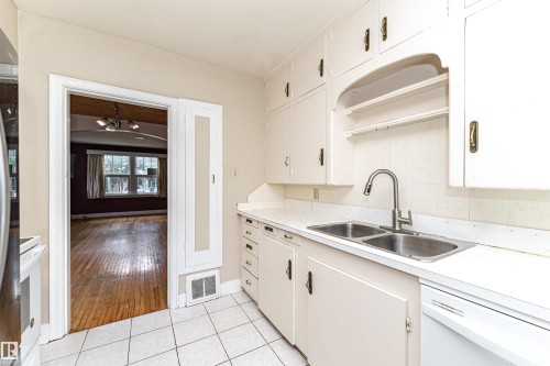 Kitchen featuring white cabinetry, a double basin stainless steel sink, a brushed nickel gooseneck faucet, and white tiled flooring - 10930 80 Avenue Nw, Edmonton, AB 