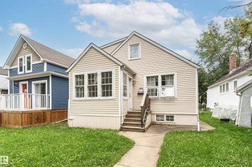 Cream-colored siding exterior with a pitched roof, front entry stairs, a concrete walkway, and a manicured lawn - 10930 80 Avenue Nw, Edmonton, AB 