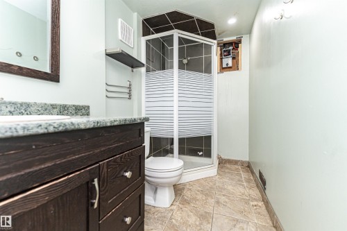 Dark wood-finish vanity with a light-toned countertop, framed mirror, and a corner shower enclosure - 10930 80 Avenue Nw, Edmonton, AB 