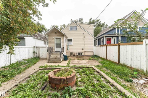 Rear exterior featuring a concrete patio, wooden stairs with metal railings, and a fenced perimeter - 10930 80 Avenue Nw, Edmonton, AB 