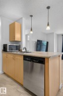 Kitchen island featuring a stainless steel dishwasher, light wood-finish cabinetry, a single basin sink with a chrome faucet, and a stone-finish countertop - 