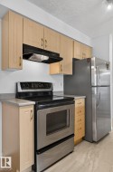 Kitchen featuring a stainless steel range with a black cooktop, stainless steel refrigerator, light wood-finish cabinetry, and solid surface countertops - 