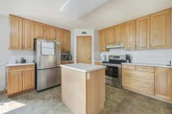 Kitchen featuring wood cabinetry with ample storage, stainless steel appliances, a central island with countertop, and tile flooring - 