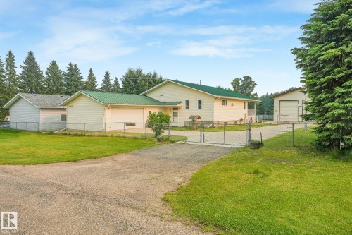 Ranch-style residence featuring a green metal roof, multiple garages, a gravel driveway, and a chain-link fence - 54 Buskmose Dr, Rural Wetaskiwin County, AB - Outdoor