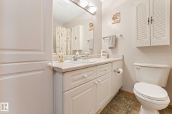 Bathroom featuring a white vanity with integrated sink, a large wall-mounted mirror, a built-in toilet, and tile flooring - 