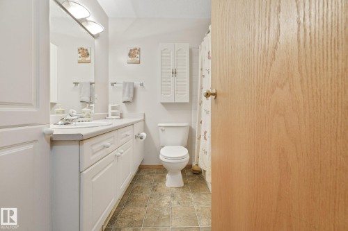Bathroom featuring a single-sink vanity with white cabinetry, a toilet, tiled flooring, and a built-in wall cabinet with louvered doors - 54 Buskmose Dr, Rural Wetaskiwin County, AB - Indoor Photo Showing Bathroom