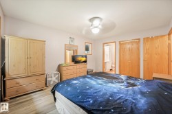 Bedroom featuring wood-finish flooring, a ceiling fan with light fixture, light-toned walls, and wood-paneled doors - 