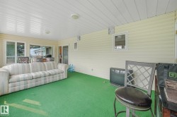 Enclosed patio featuring light-colored vinyl siding, a white paneled ceiling with flush-mount lighting, and a green carpeted floor - 