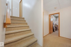 Carpeted staircase with a natural wood handrail, leading to an upper landing featuring carpeted flooring and a solid wood door frame - 