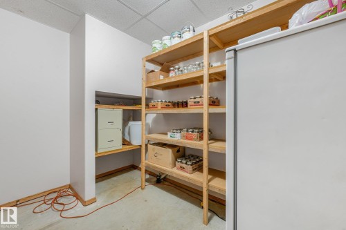 Dedicated storage room featuring extensive wood shelving, a built-in nook with shelving, and concrete flooring - 54 Buskmose Dr, Rural Wetaskiwin County, AB - Indoor