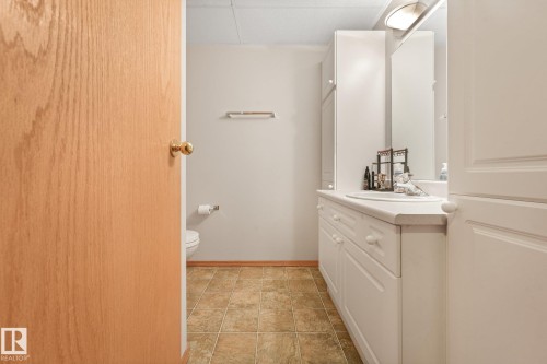Bathroom featuring a light wood-finish door, tile flooring, white vanity with integrated sink, overhead lighting, and wall-mounted mirror - 54 Buskmose Dr, Rural Wetaskiwin County, AB - Indoor Photo Showing Bathroom
