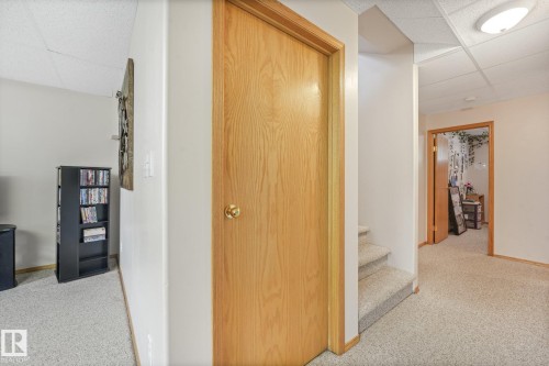 Carpeted hallway with a light wood-finish door, matching trim, and a drop ceiling with recessed lighting - 54 Buskmose Dr, Rural Wetaskiwin County, AB - Indoor Photo Showing Other Room