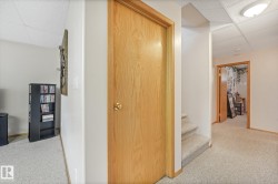 Carpeted hallway with a light wood-finish door, matching trim, and a drop ceiling with recessed lighting - 