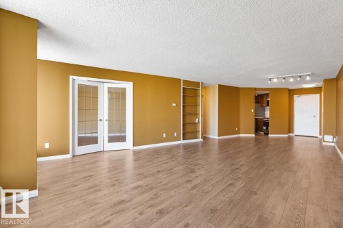 Expansive room featuring wood-finish flooring, track lighting, built-in shelving, and French doors with glass panels - #1307 10045 117 St Nw, Edmonton, AB 