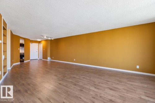 Spacious living area featuring wood-finish flooring, built-in shelving, track lighting, and a textured ceiling - #1307 10045 117 St Nw, Edmonton, AB 