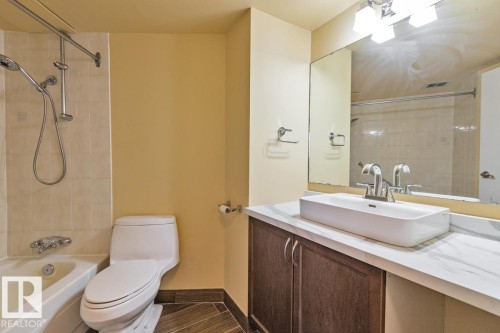 Bathroom featuring a combination shower and tub with tiled surround, a white rectangular vessel sink, a wood-finish vanity, and wood-look flooring - #1307 10045 117 St Nw, Edmonton, AB 