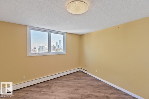 Window with urban skyline, wood-finish flooring, ceiling-mounted light fixture, and neutral wall paint - #1307 10045 117 St Nw, Edmonton, AB 