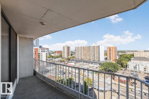 Concrete balcony with metal railing, featuring city buildings and distant green spaces - #1307 10045 117 St Nw, Edmonton, AB 