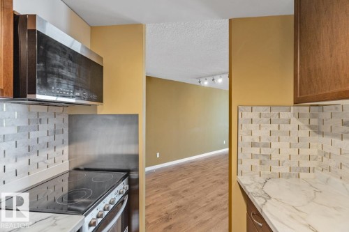 Kitchen featuring a built-in microwave, electric range, tile backsplash, and stone-finish countertops - #1307 10045 117 St Nw, Edmonton, AB 