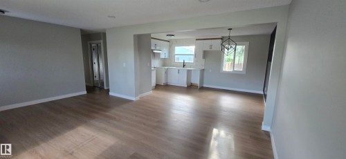 Open-concept layout with wood-finish flooring, white kitchen cabinetry, recessed lighting, and a modern geometric pendant light fixture - 13812 63 Street Nw, Edmonton, AB 