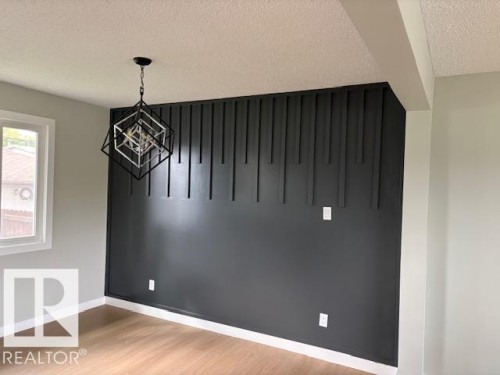 Accent wall with vertical paneling, contemporary geometric pendant light, wood-finish flooring, and white trim - 13812 63 Street Nw, Edmonton, AB 