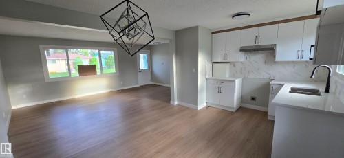 Open-concept living area with wood-finish flooring, a contemporary geometric chandelier, and white trim - 13812 63 Street Nw, Edmonton, AB 