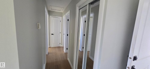 Hallway featuring wood-finish flooring, white paneled doors with matte black hardware, and mirrored closet doors - 13812 63 Street Nw, Edmonton, AB 