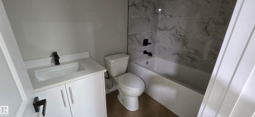 Bathroom featuring a white vanity with integrated sink, matte black faucet, and a tiled shower-over-tub with matte black fixtures - 13812 63 Street Nw, Edmonton, AB 