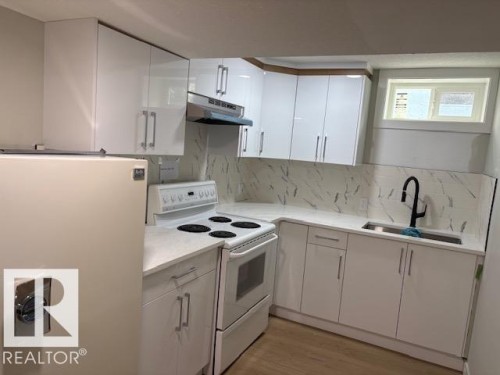 White flat-panel cabinetry with metal hardware, white countertop surfaces, white tile backsplash, and wood-finish flooring - 13812 63 Street Nw, Edmonton, AB 