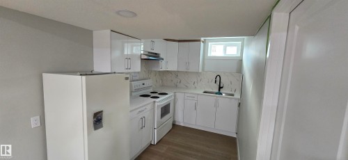 Modern kitchen featuring white cabinetry, a black faucet, a built-in electric range, a refrigerator, and wood-finish flooring - 13812 63 Street Nw, Edmonton, AB 