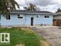 Light blue stucco exterior with white-framed windows, dark shingle roof, and concrete foundation - 13812 63 Street Nw, Edmonton, AB 