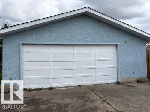 Attached garage featuring a panel-style door, textured exterior finish, and a sloped roofline - 13812 63 Street Nw, Edmonton, AB 