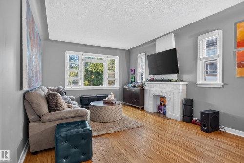 Hardwood flooring, painted gray walls, white trim details, multiple windows, and a decorative fireplace with a mantle - 11406 83 Street Nw, Edmonton, AB 