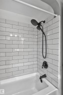 Subway tile shower surround with dark grout, dual-head shower fixture in an oil-rubbed bronze finish, and a white bathtub - 