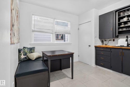 White subway tile backsplash, wood-finish countertops, black cabinetry with gold-tone hardware, light-toned tile flooring, and a built-in bench - 11406 83 Street Nw, Edmonton, AB 