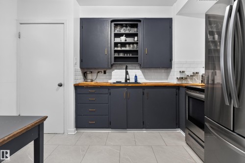 Dark cabinetry with gold-tone hardware, wood-finish countertops, white subway tile backsplash, and stainless steel appliances - 11406 83 Street Nw, Edmonton, AB 