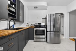 Updated kitchen featuring stainless steel appliances, dark cabinetry, wood-finish countertops, subway tile backsplash, and light tile flooring - 