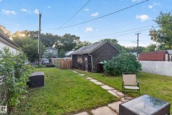 Expansive backyard featuring a stone paver pathway, a detached shed with wood shingle siding, and a white lattice fence - 