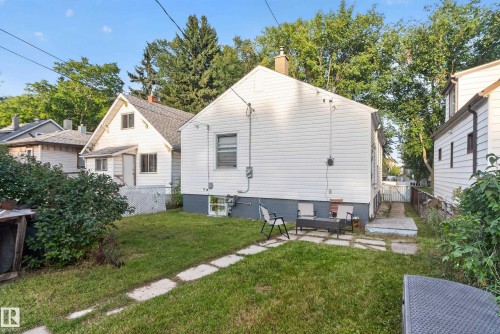 Rear exterior featuring white siding, a stone patio, and a grass lawn - 11406 83 Street Nw, Edmonton, AB 