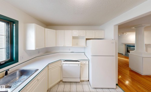 White kitchen cabinetry, white countertops, stainless steel sink, white tile flooring, and a white refrigerator - 10941 81 Avenue Nw, Edmonton, AB 